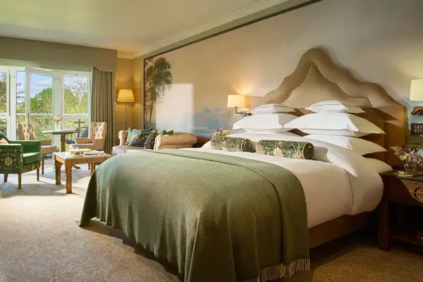 A wellappointed hotel room featuring a large bed with multiple pillows and a sitting area by glass doors leading to an outdoor view