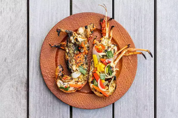 Grilled lobster halves garnished with vegetables on a plate, served on a wood table