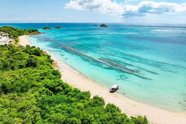Aerial view of a tropical beach with lush greenery, turquoise waters, and a small boat on the shore