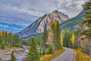 A mountain with a winding road and forest in the foreground