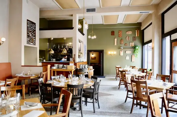 Interior of a casual restaurant with wooden tables and chairs scenic decor and an open kitchen area visible
