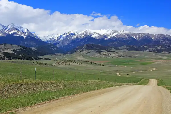 A dirt road stretching into a valley with a mountainous backdrop