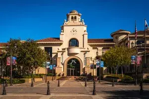 Spanishstyle municipal building with a distinctive clock tower arched entrance and decorative banners along the walkway