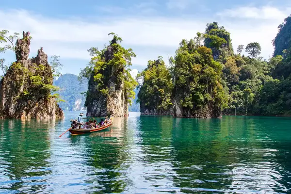 boat of people in water drifting between tall natural rock formations out of water