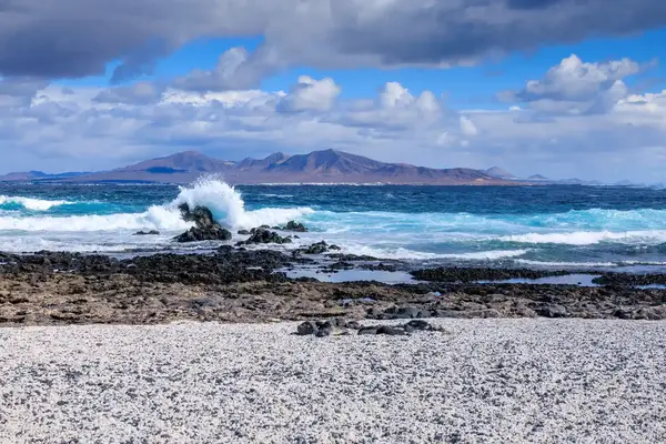 A rocky beach with waves crashing against stones a distant island visible across the water