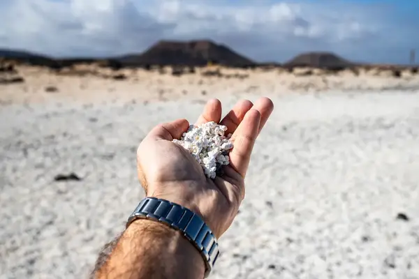 A hand holding white stones in a desertlike landscape with mountains in the background