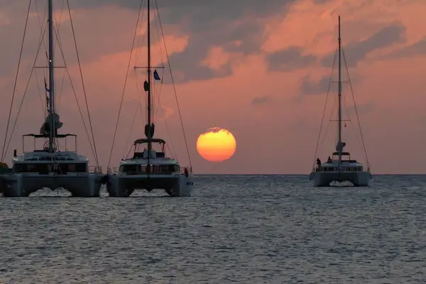 The sun is nearing the horizon in this sunset scene of catamarans on the water off Anguilla.
