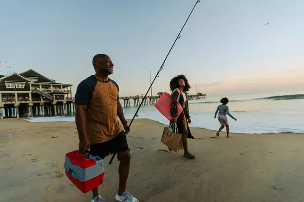 Horizontal shot of family walking along the water holding fishing pole and picnic things. Pier in the background taken at sunrise in the Outer Banks