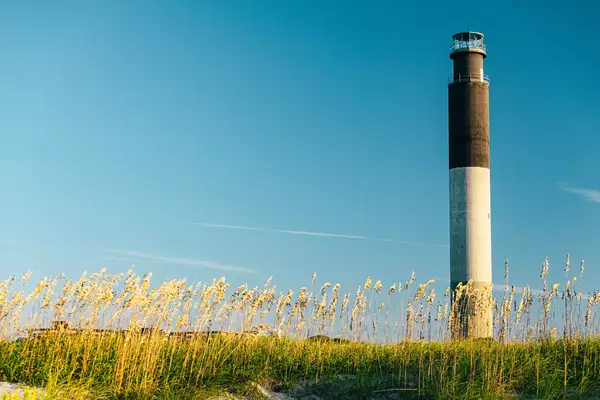 Oak Island lighthouse pictured in soft morning light with dunes surrounding structure.