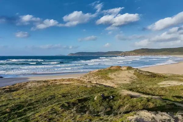 Waves are seen crashing into the rugged shore of Rostro Beach in Fisterra, Galicia, Spain, from the vantage point of a grassy hill nearby.