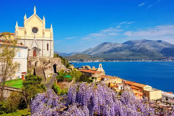 Gaeta, Italy, blooming wisteria flowers and historical churches of St Francis of Assisi and Santissima Annunziata over the blue waters of the bay of Gaeta