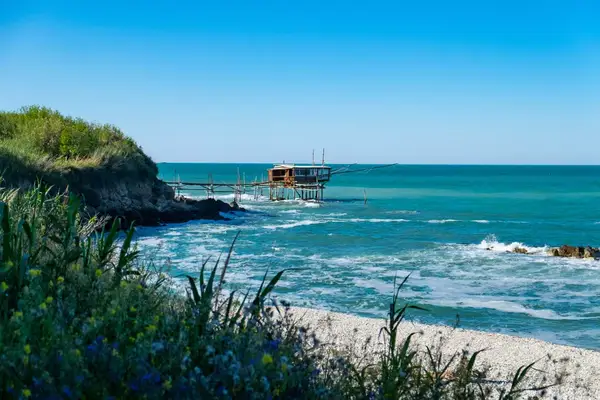 a traboccho in the San Vito Marina is seen in the distance over a pebbly beach with blue water