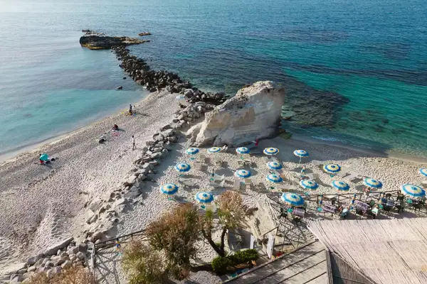 Aerial drone view of people relaxing on a sandy beach with beach umbrellas in Tropea on the Tyrrhenian coast of Italy