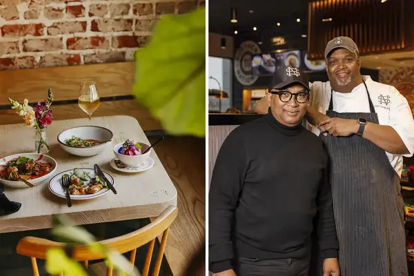 Two chefs posing together in a restaurant a set table with dishes in the background
