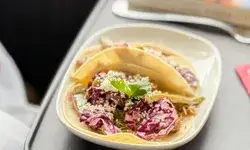 Three tacos on a plate with a garnish placed on a tray table
