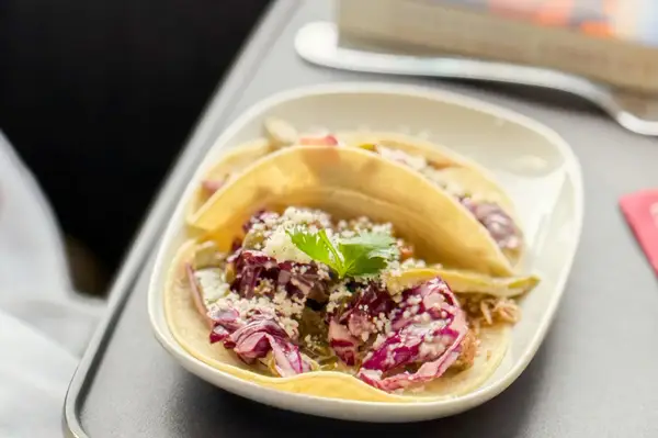 Three tacos on a plate with a garnish placed on a tray table