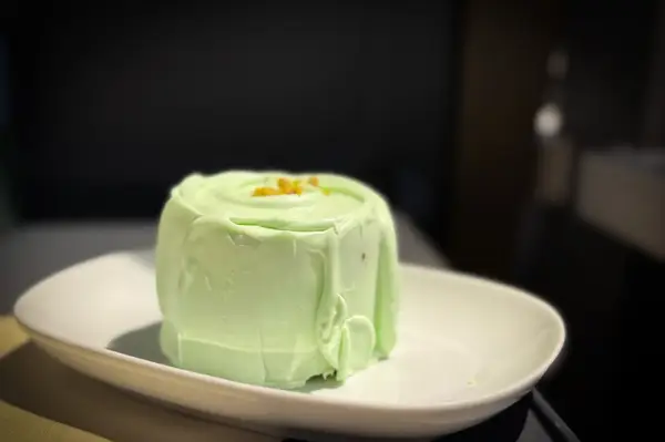 A green mousse dessert on a white plate with a garnish on top