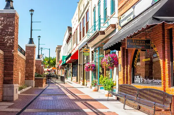 A town street with brick pavement storefronts benches and hanging flower baskets