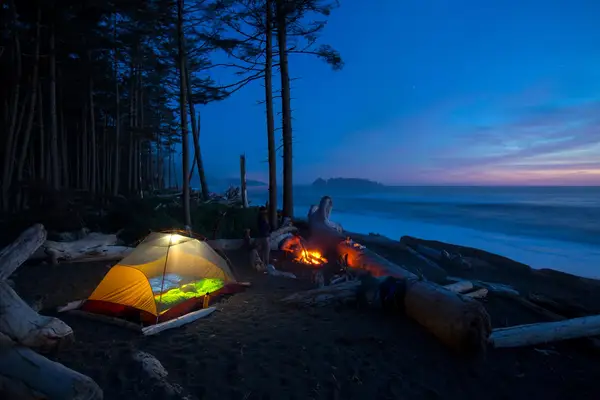 A camping tent and a campfire on a beach near the ocean at sunset