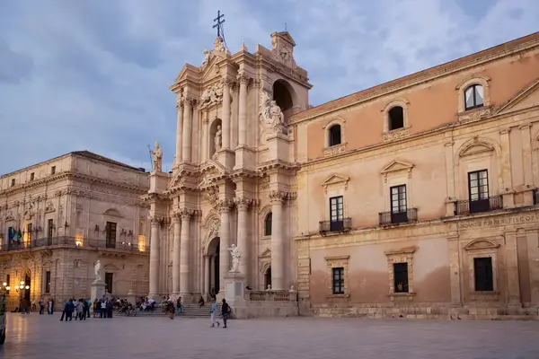 Historical building in an open square with people walking and gathering likely in Ortigia Italy