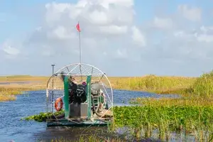 An airboat navigating through the wetlands of Everglades National Park, with tall grass and water surrounding it