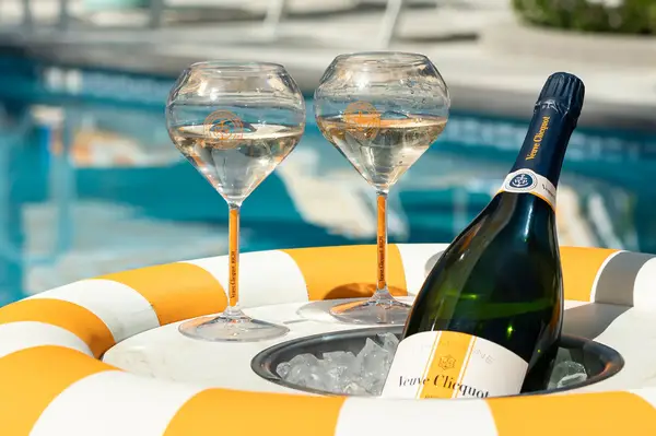 Two wine glasses and a bottle of Veuve Clicquot in a poolside setting