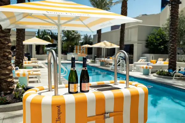 Poolside area with a yellow and white striped bar and champagne bottles on top, surrounded by parasols and lounge chairs