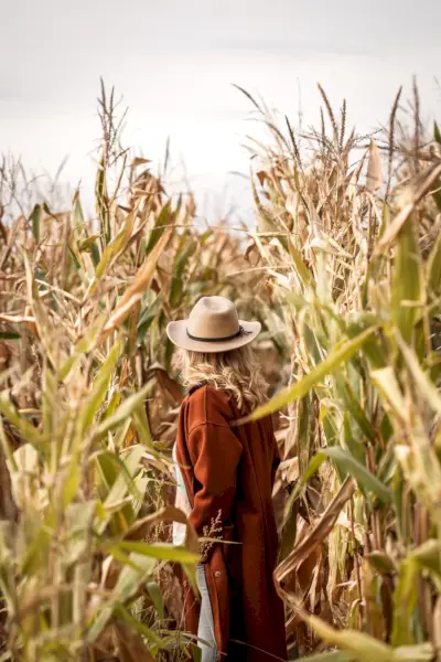 stylish woman wearing red coat and hat is standing in maize field