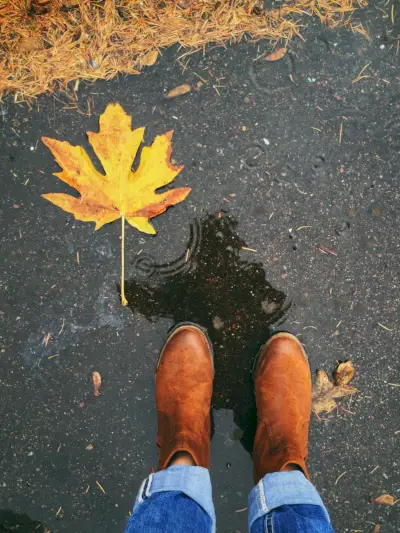 womans reflection in a puddle holding an autumn leaf
