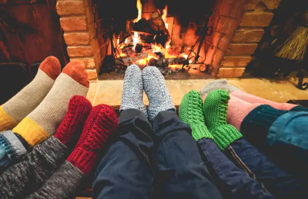 legs view of happy family wearing warm socks in front of fireplace winter, love and cozy concept focus on center grey woolen socks