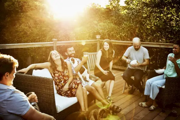 adult friends, men and women, hanging out on deck, laughing, drinking, eating, possibly asking never have i ever questions