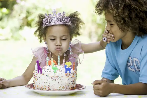 cute girl in crown blowing out candles and covering brother