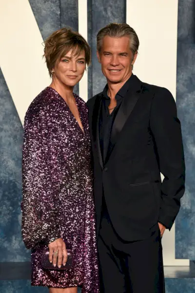 olyphant in a stylish all black suit and and knief in a plum colored long sleeved sequin mini dress