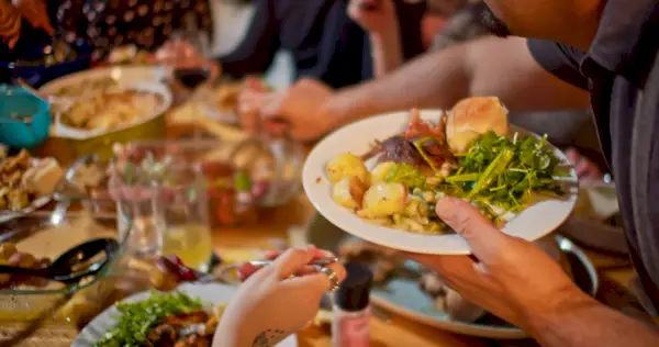 man serving himself at a dinner table, there are greens and a biscuit on his plate