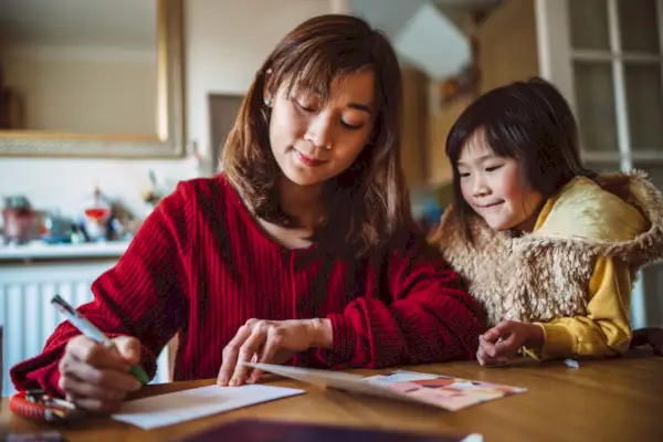 young pretty mom writing greeting card for family with her lovely daughter at home