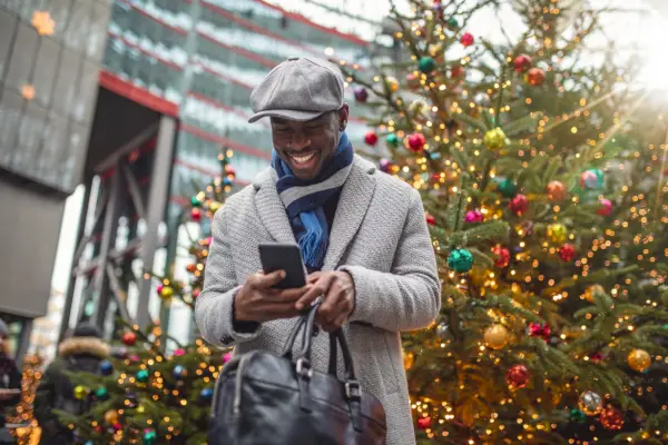 handsome and beautiful black businessman standing on the street in winter coat taking selfies with christmas trees