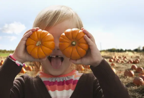 caucasian girl covering eyes with small pumpkins