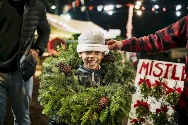 smiling boy wearing christmas wreath while shopping for tree with family