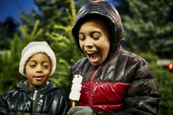 smiling boy about to eat snowman shaped marshmallow while shopping for christmas tree