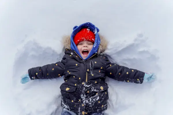 young child in snow making snow angel