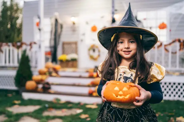 little girl in witch costume holding jack o lantern pumpkins on halloween trick or treat