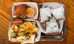 A tray with beignets covered in powdered sugar and sandwiches in white paper containers