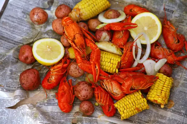 A crawfish boil spread with potatoes corn on the cob onions and lemon slices on newspaper