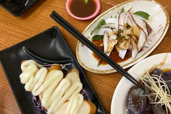 A variety of plated food items on a wooden table in a restaurant featuring a dish of squid bread with mayonnaise and eggplant with sauce