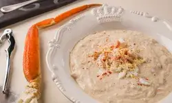 A bowl of creamy crab soup garnished with shredded crab meat and spices accompanied by a crab leg and a nutcracker