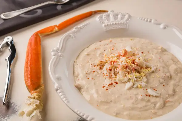 A bowl of creamy crab soup garnished with shredded crab meat and spices accompanied by a crab leg and a nutcracker