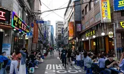 A bustling street scene in Seoul South Korea with people dining at outdoor tables and neon signs on buildings