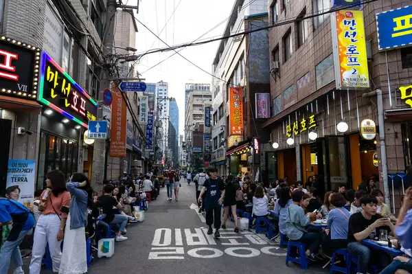 A bustling street scene in Seoul South Korea with people dining at outdoor tables and neon signs on buildings