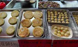 Various trays of food items including panfried pancakes and dumplings displayed on a counter