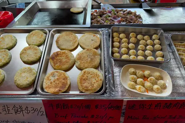 Various trays of food items including panfried pancakes and dumplings displayed on a counter